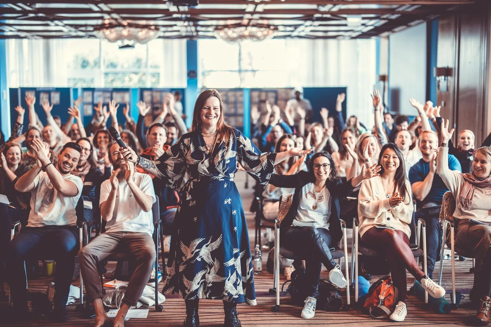 Melanie mit Mikrofon vor vollem Saal, das Publikum streckt lachend die Hände in die Höhe