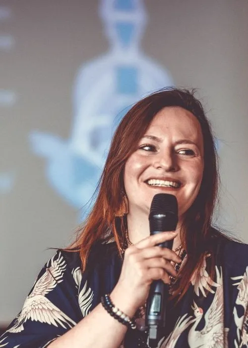 Melanie Dorn lacht und spricht mit Mikrofon bei einem Vortrag